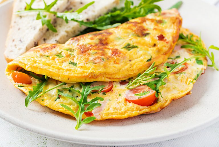 Omelette with tomatoes, ham, cheese and green herbs on plate. Frittata - italian omelet.